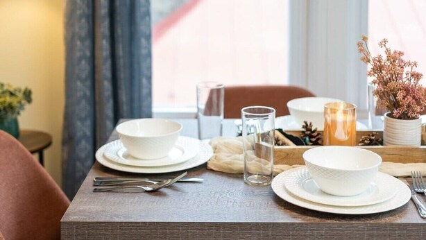 Mesa lista con platos, vasos y cubiertos, con vista a un edificio de techos rojos.