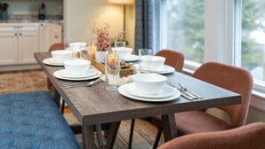 Un comedor con mesa de madera dispuesta para cuatro, platos blancos y un florero con flores.