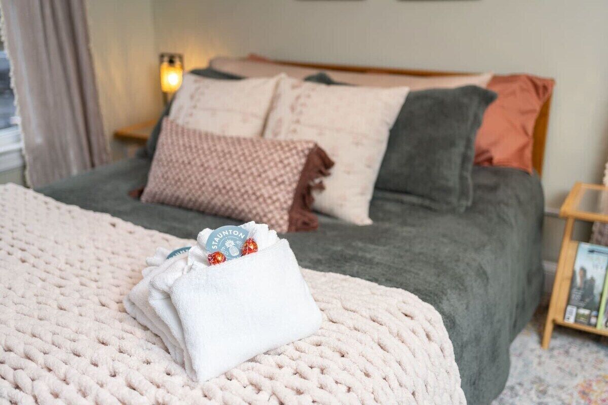 Una cama bien hecha con una manta blanca y una pequeña bolsa blanca encima.