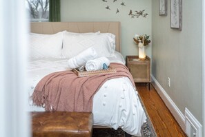 A neatly made bed with white linens and a pink throw blanket, a bedside table with a vase of flowers, and a wall with bird decals. - The Nest: Cozy Staunton Apartment + Walk Downtown (Staunton)