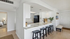 A modern kitchen with a central island, bar stools, and white cabinetry.