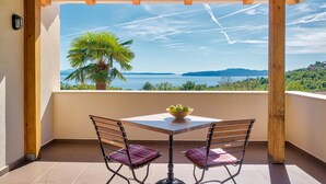 A balcony with two chairs, a table, and a bowl of fruit. A palm tree and a view of the sea and hills are visible. - Lovely home in Opatija (Opatija)