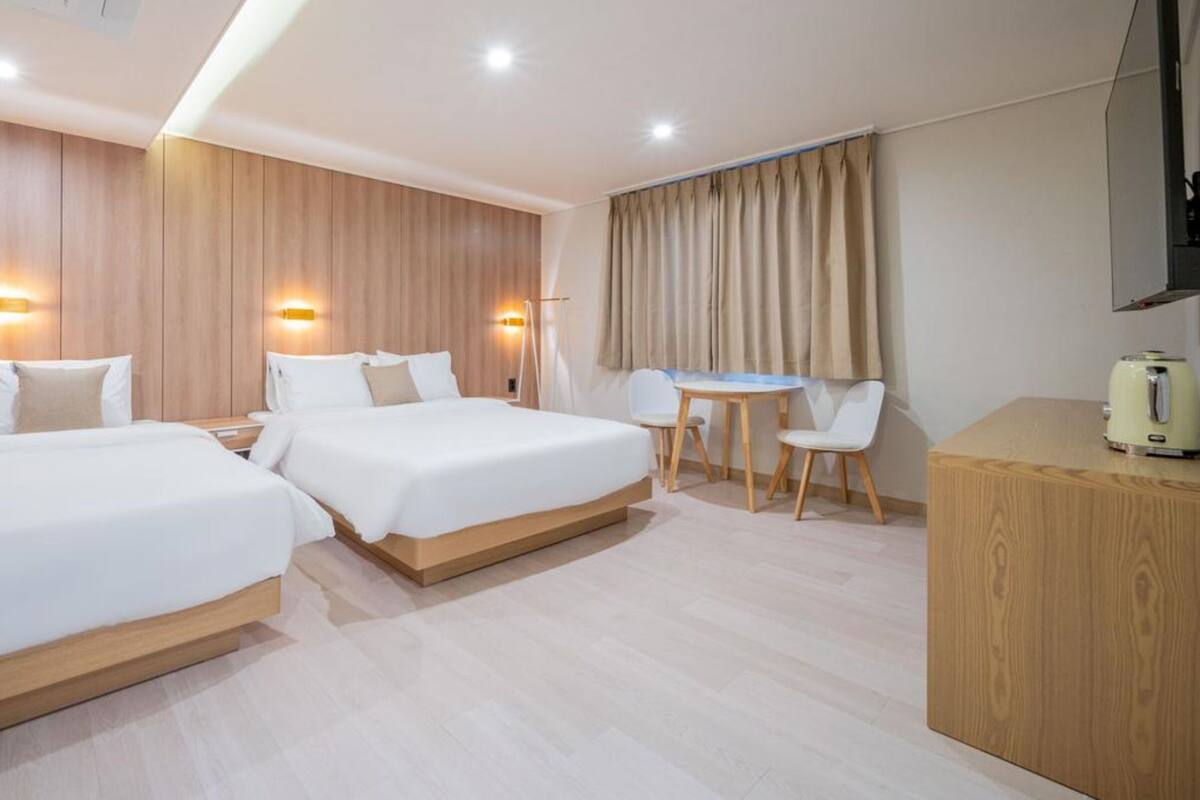 A hotel room with two beds, a desk, a chair, and a coffee machine.