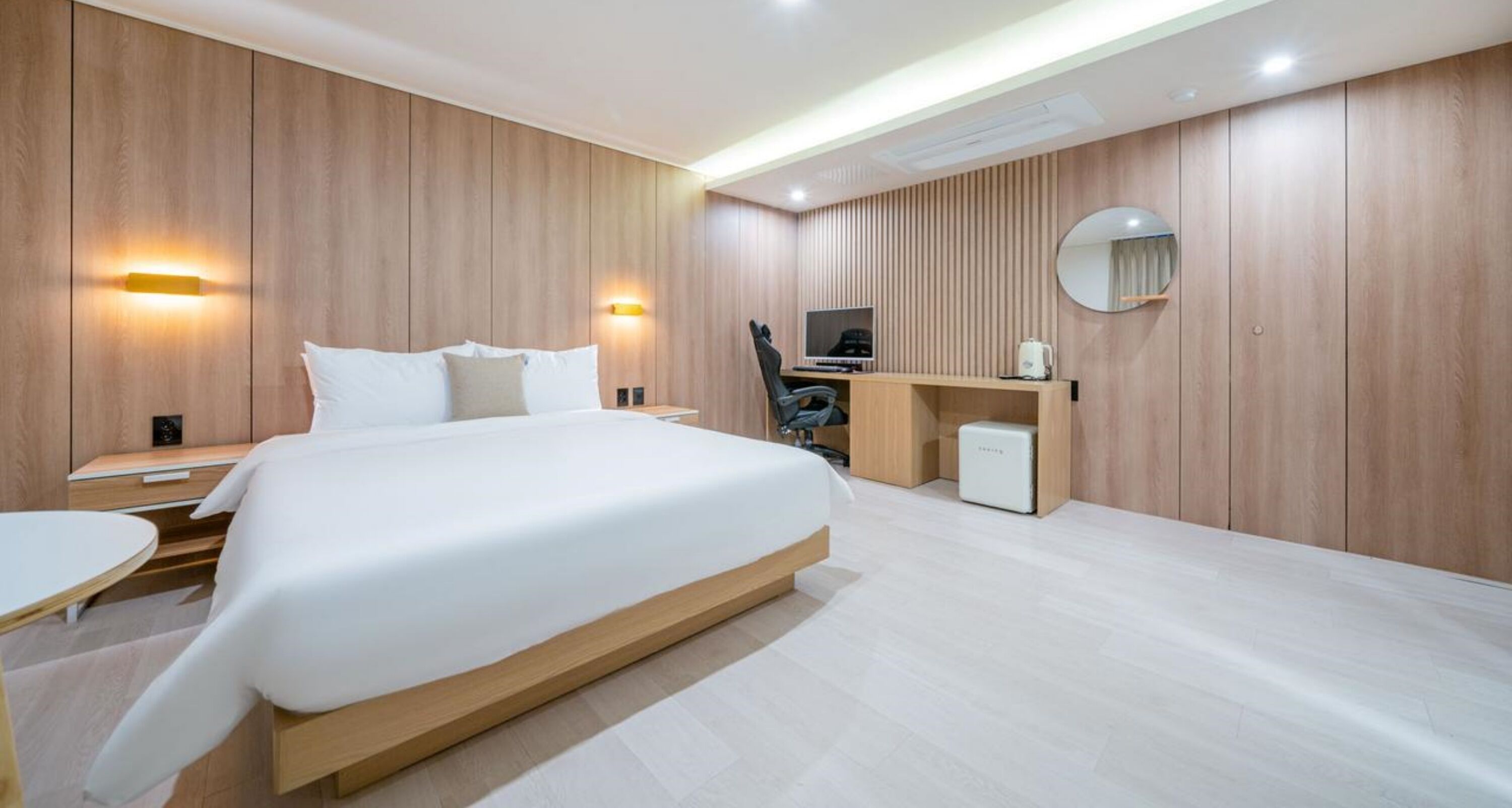 Une chambre d’hôtel moderne dotée d’un grand lit, de tables de chevet, d’un bureau avec une chaise, d’un petit réfrigérateur et d’une télévision.