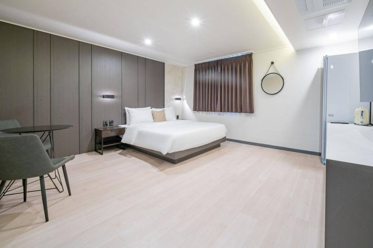 A modern hotel room with a bed, bedside table, chair, and a small table.