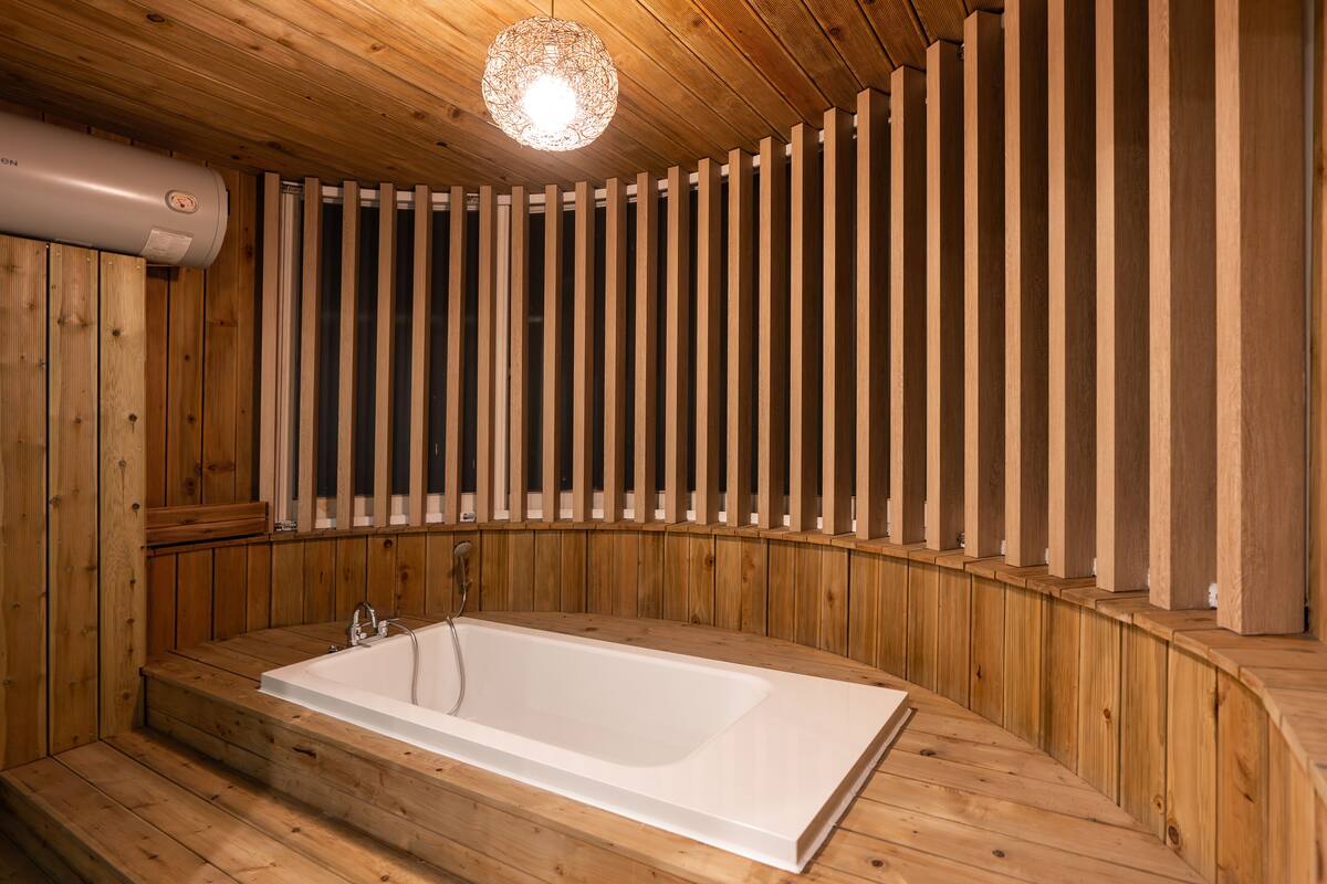 A wooden spa with a large bathtub, wooden paneling, and a hanging light fixture.