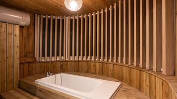 Un espace de bien-être en bois, doté d’une grande baignoire, de lambris en bois et d’un luminaire suspendu.