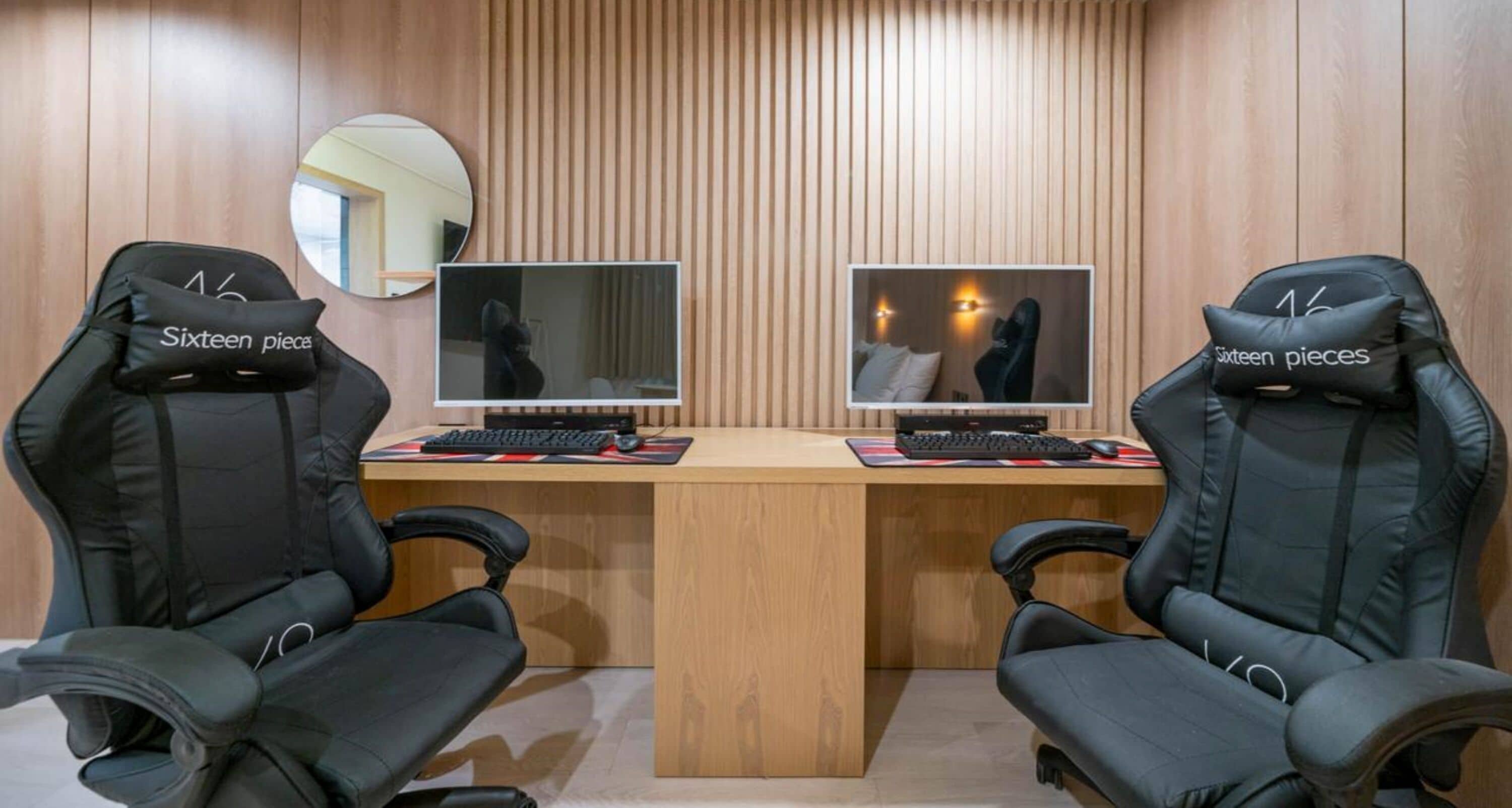 Un espacio de oficina moderno con dos sillas de juego negras con la etiqueta “Sixteen pieces” y un escritorio de madera con dos monitores de computadora.