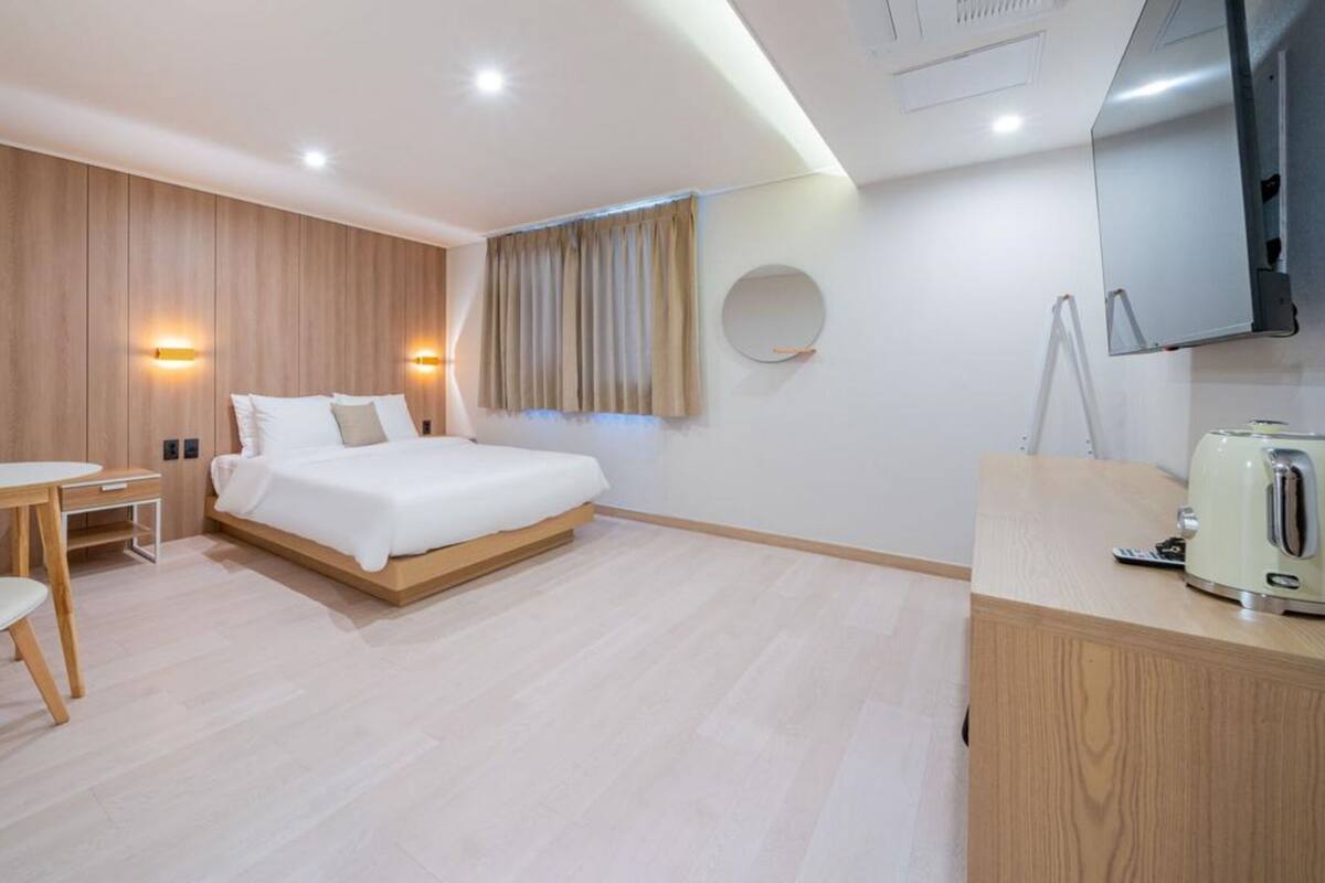 A modern hotel room with a bed, a desk, a chair, a round mirror, and a television.
