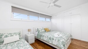 A bedroom with two beds, a ceiling fan, a window, and a wardrobe.