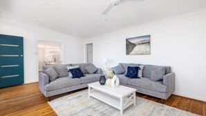 A modern living room with a grey sofa set, a white coffee table, and a beach-themed painting on the wall.