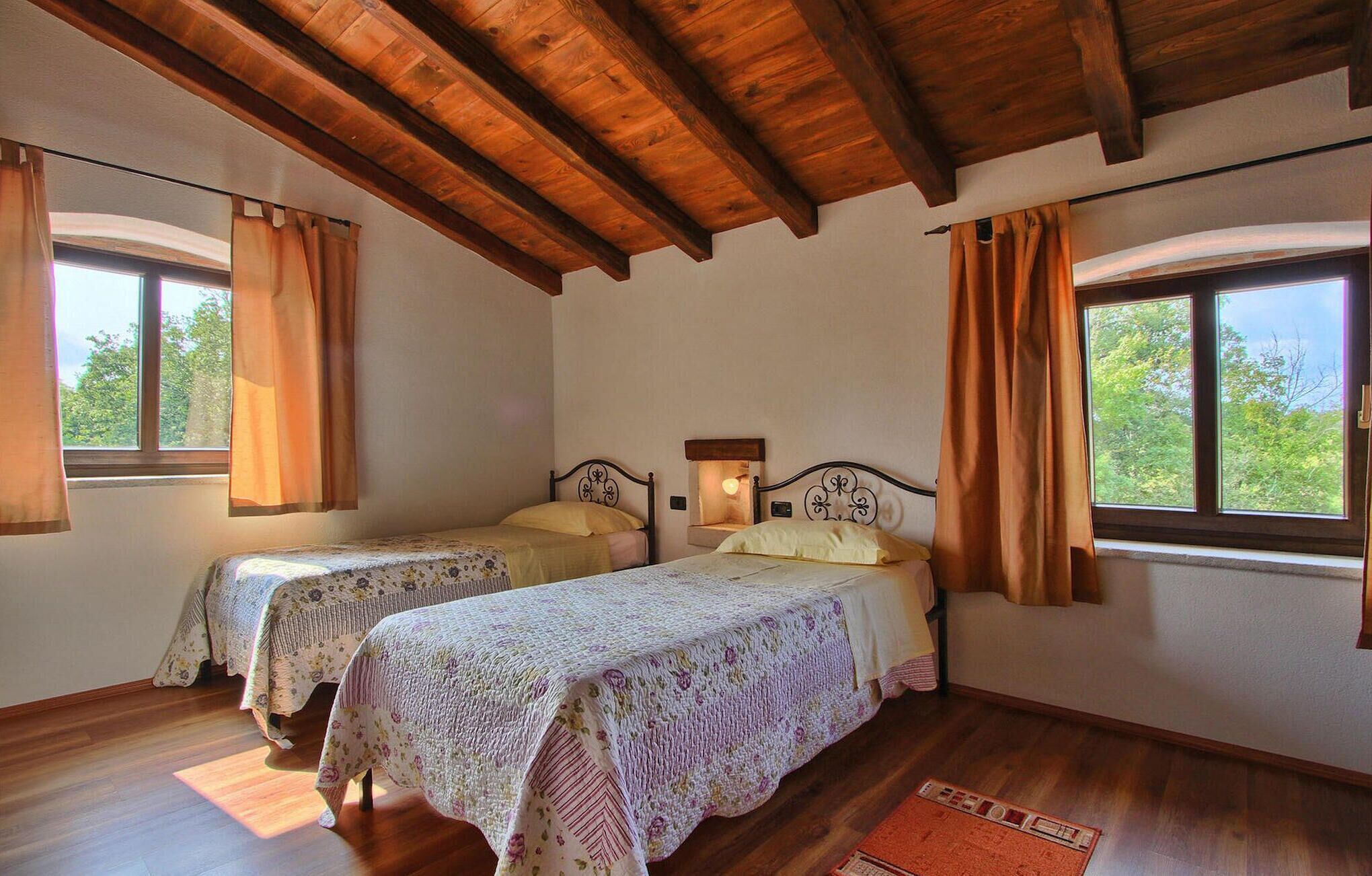 Quarto com duas camas, vigas de madeira no teto e grandes janelas com cortinas.