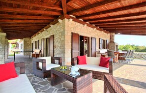 A covered outdoor seating area with wicker furniture, stone walls, and wooden beams. - Amazing home in Tinjan (Tinjan)