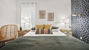Une chambre moderne avec un grand lit, deux tables de chevet, une chaise et un mur orné d’un motif de feuilles.
