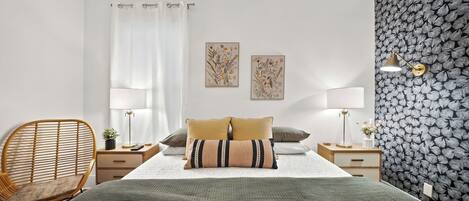 A modern bedroom with a large bed, two bedside tables, a chair, and a wall with a leaf pattern.