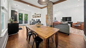 Un espace de vie moderne comprenant une table à manger en bois, des chaises noires, un canapé gris et un téléviseur.