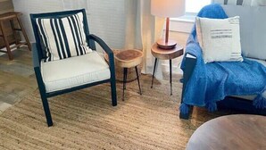 Una habitació amb una cadira estriada, una cadira blava amb una manta, una taula rodona petita i una làmpada.
