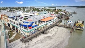 A waterfront hotel with a pier extending into the water, featuring multiple levels with outdoor seating and a view of the sea. - Beachfront Bliss - King Bed - Heated Pool - Steps to John’s Pass & Dining! (Madeira Beach)