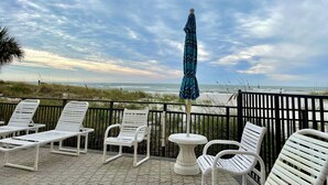 A beachside patio with white lounge chairs and a table, overlooking the ocean. - Beachfront Bliss - King Bed - Heated Pool - Steps to John’s Pass & Dining! (Madeira Beach)