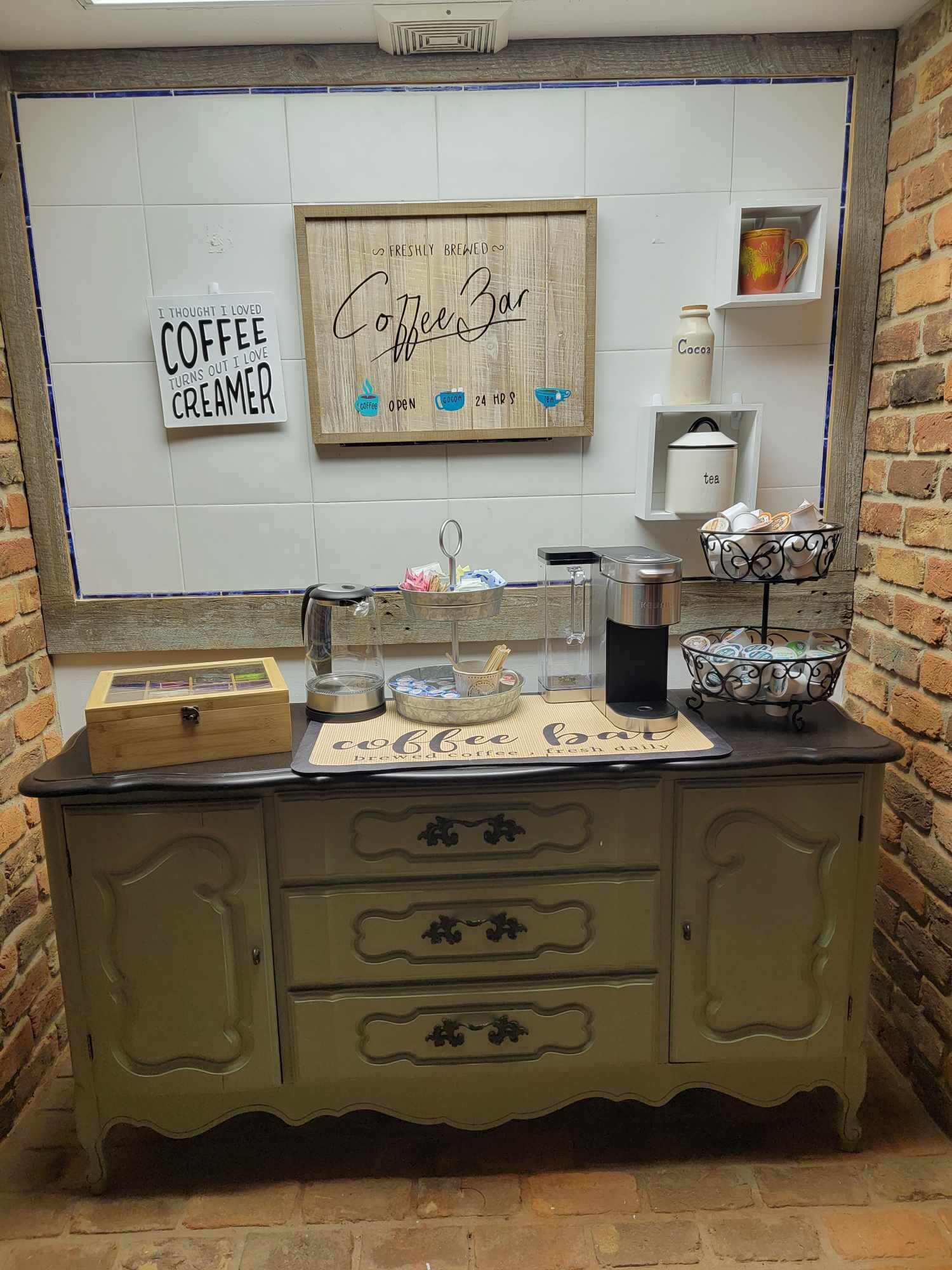 Un angolo caffetteria con un cartello che recita “Caffetteria con caffè appena preparato” e un altro che dice “Pensavo di amare i gusti per il caffè”. Si vedono attrezzature per la preparazione del caffè, un macinino e una caffettiera sul bancone.