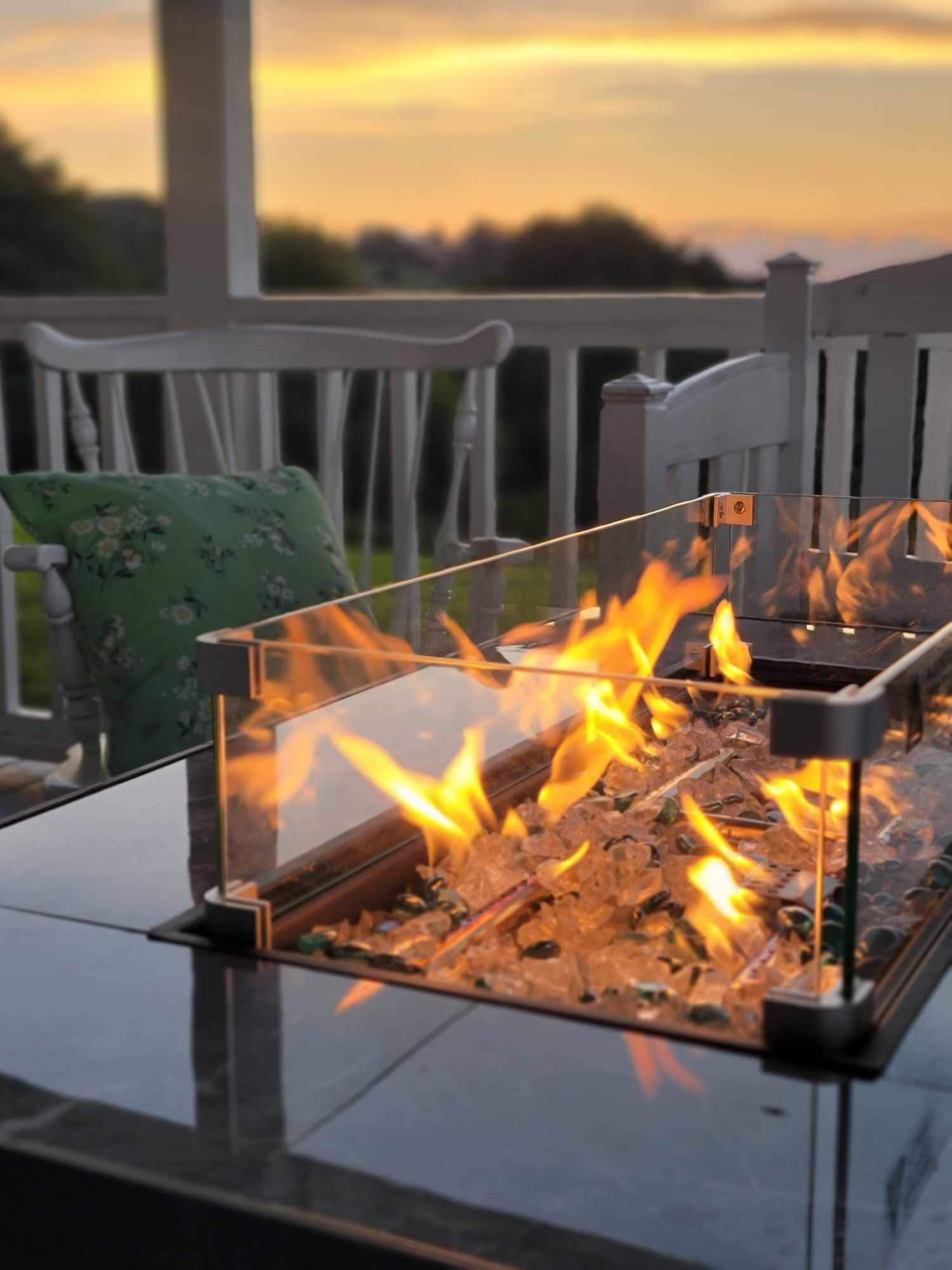 A glass-top table with a metal fire feature containing burning wood.
