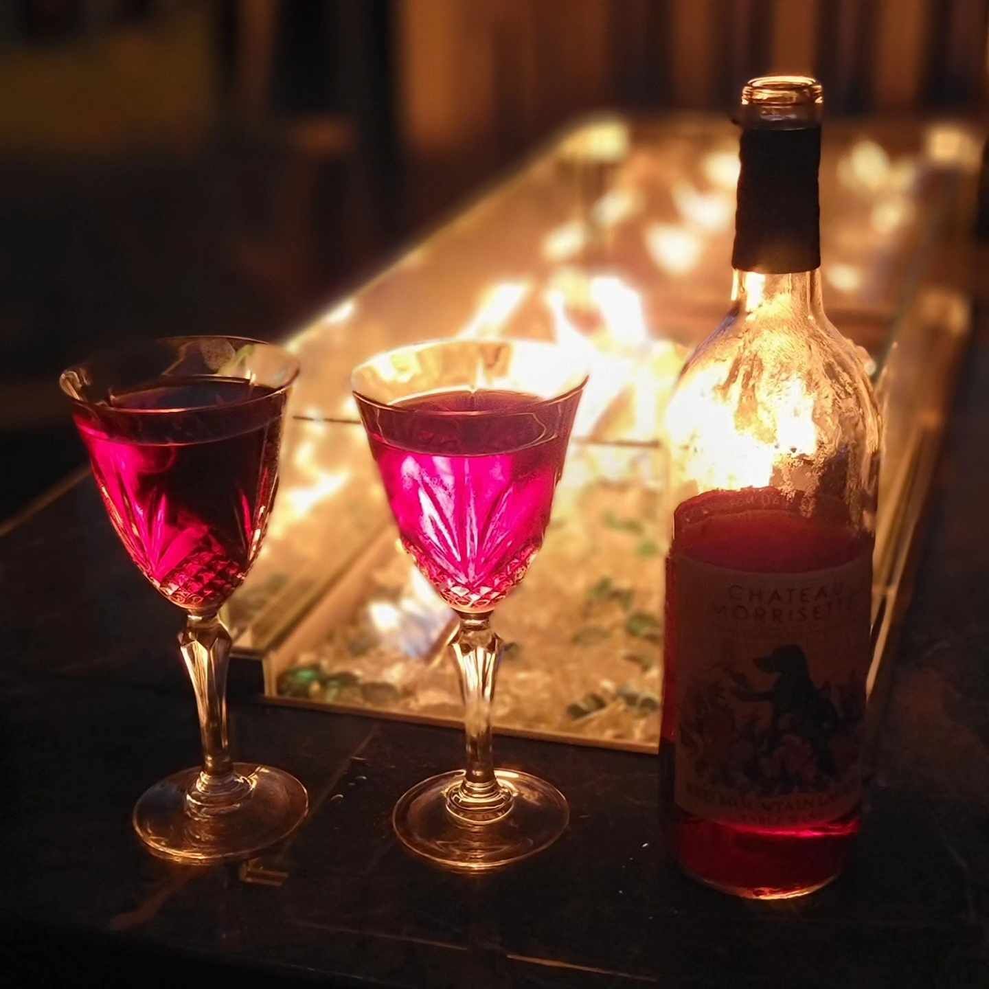 A bottle of Chateau d'Orrièset wine and two glasses on a table with a warm light source in the background.