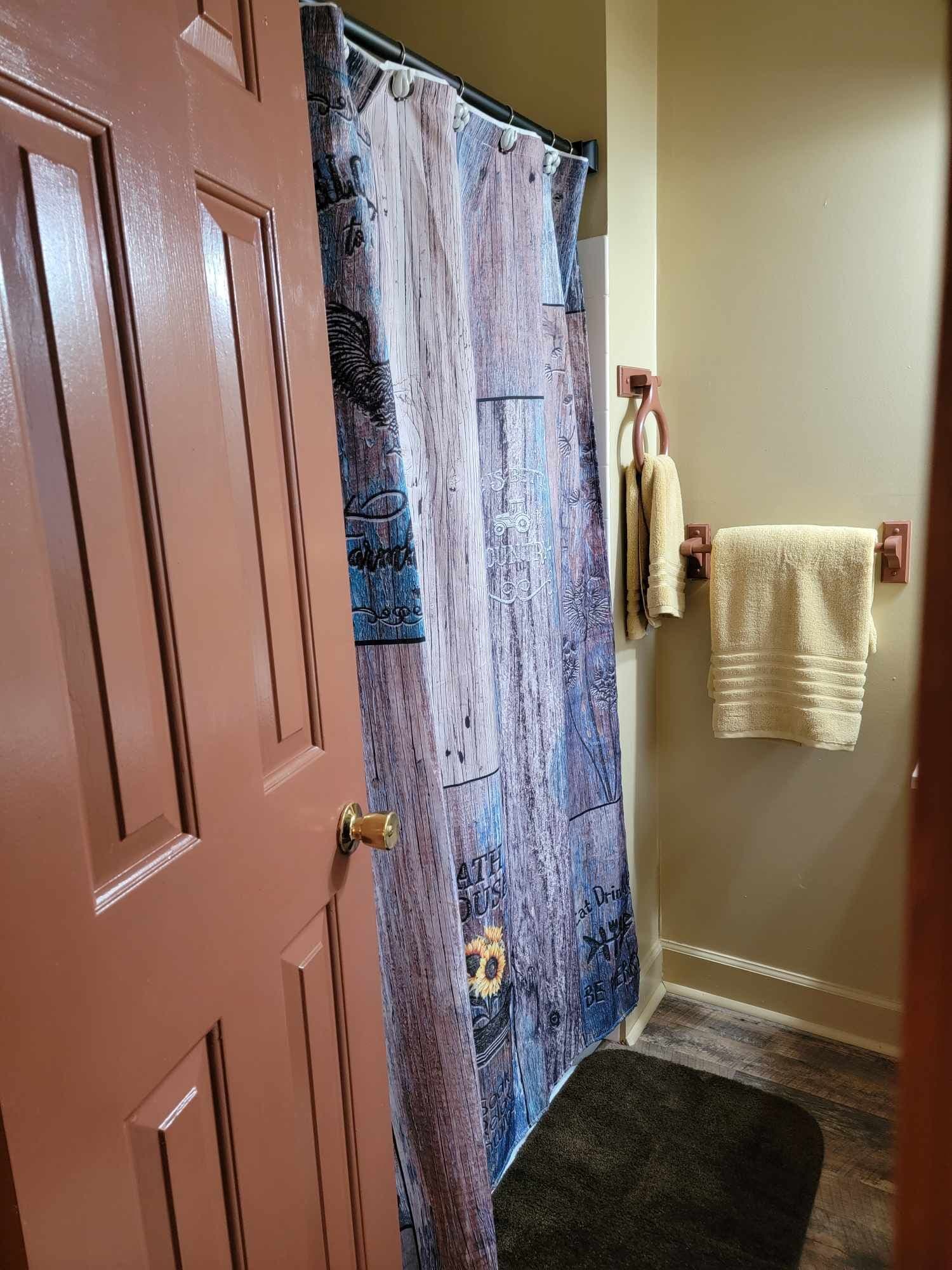 A bathroom with a shower curtain featuring a floral design, a towel rack with a towel, and a door.