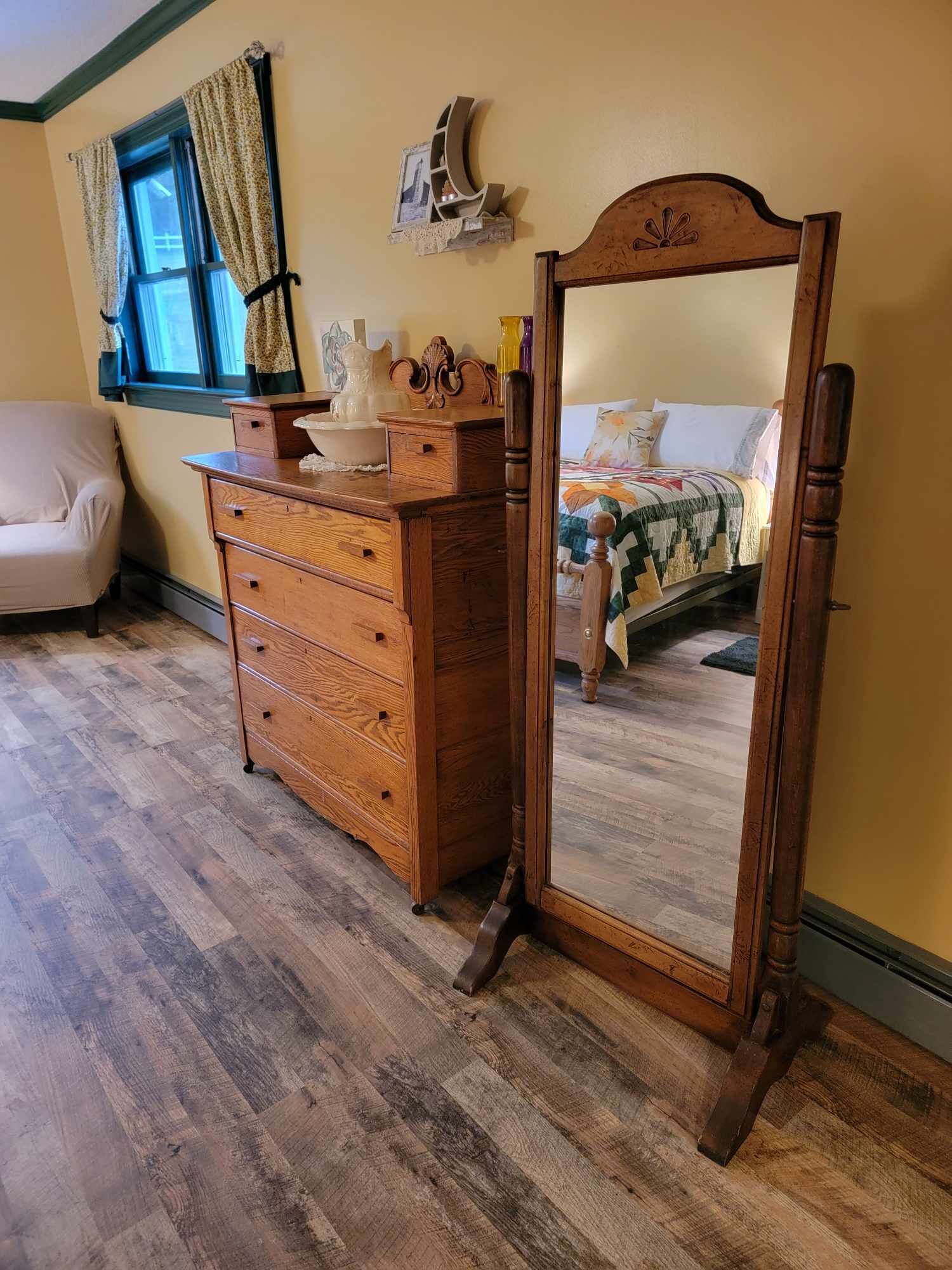 Een kamer met een houten dressoir, een spiegel, een bed met quilt en een stoel.