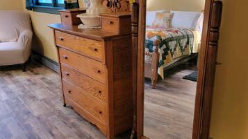 Een kamer met een houten dressoir, een spiegel, een bed met quilt en een stoel.