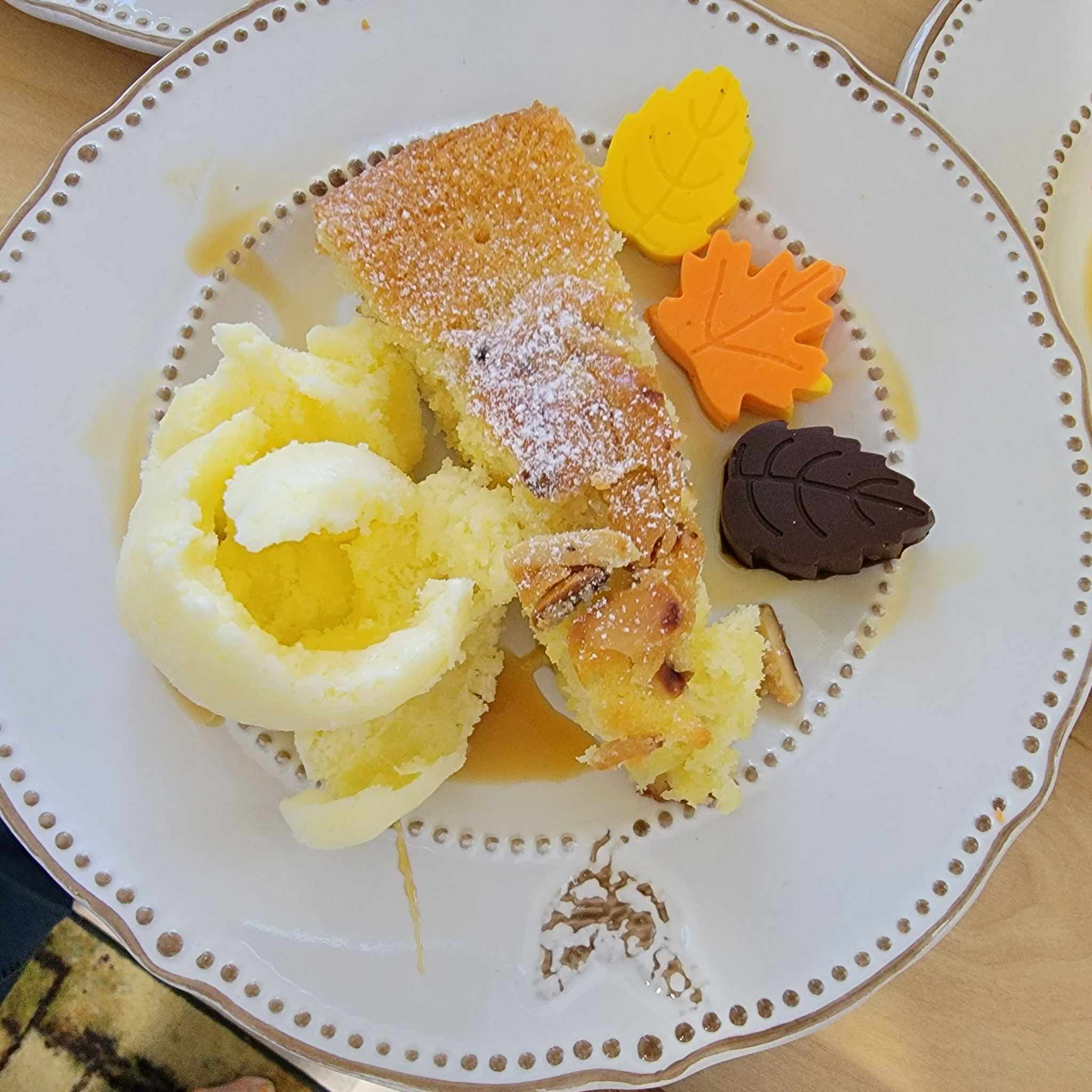 Un plato con una porción de pastel, una bola de helado y dos galletas con forma de hoja.