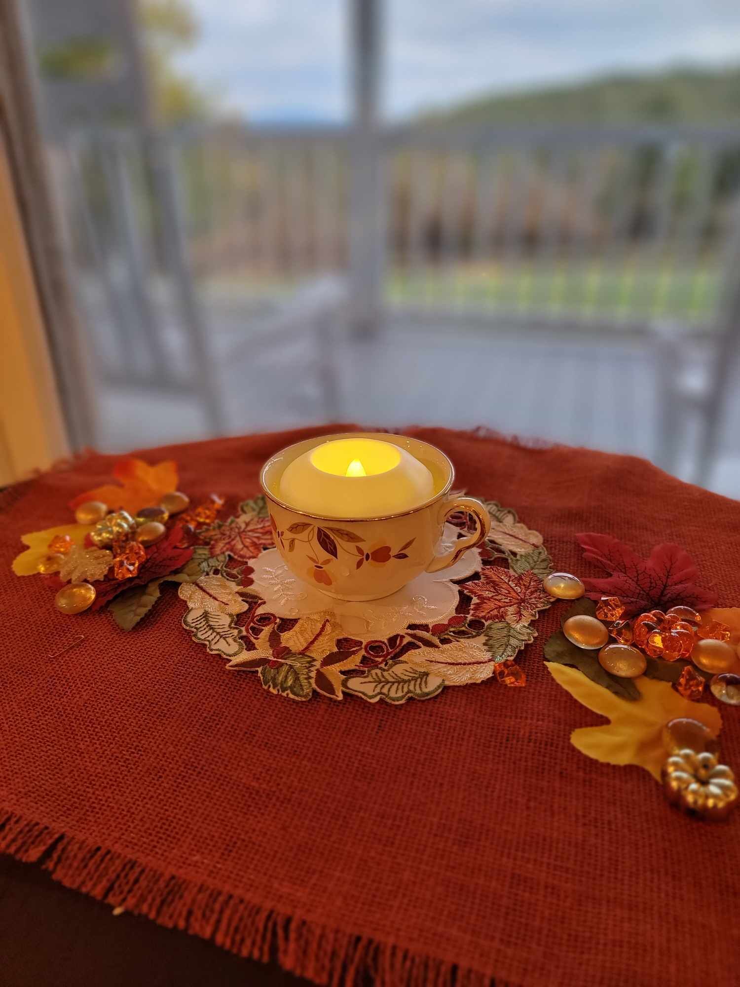 A candle in a decorative cup on a table with a red cloth.