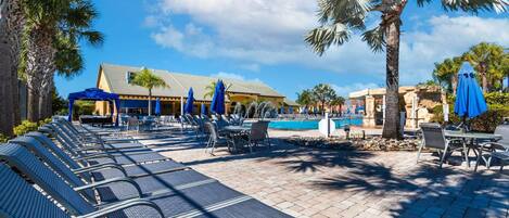 A poolside area with lounge chairs, umbrellas, and a building with a tiled roof.