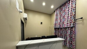 Un hall d’hôtel avec un comptoir d’accueil blanc, des murs de couleur beige et des rideaux à motifs.
