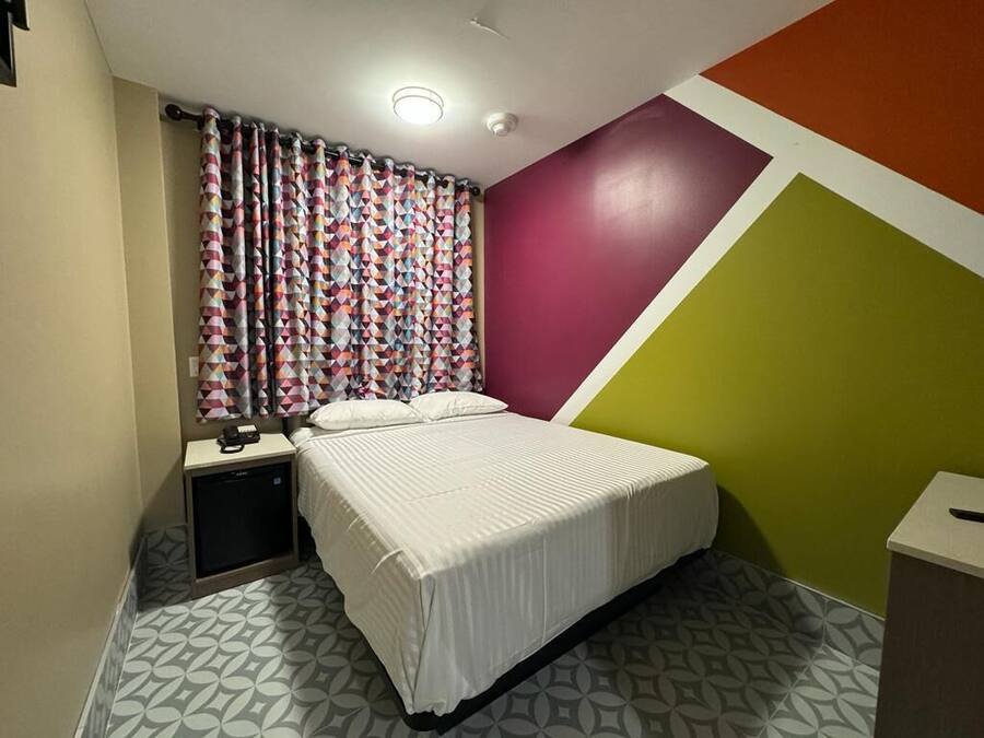 Een slaapkamer met een bed, nachtkastje, televisie en een muur met een geometrisch patroon.