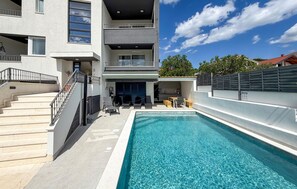 A modern building with a pool, outdoor seating, and a staircase leading to the entrance.