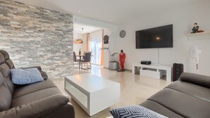 Un salon moderne avec un mur d’accent en pierre, un téléviseur à écran plat et un coin repas comprenant une table et des chaises.