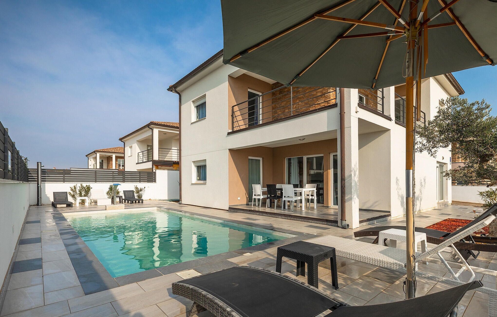 A modern two-story house with a swimming pool, outdoor seating, and a covered patio area.