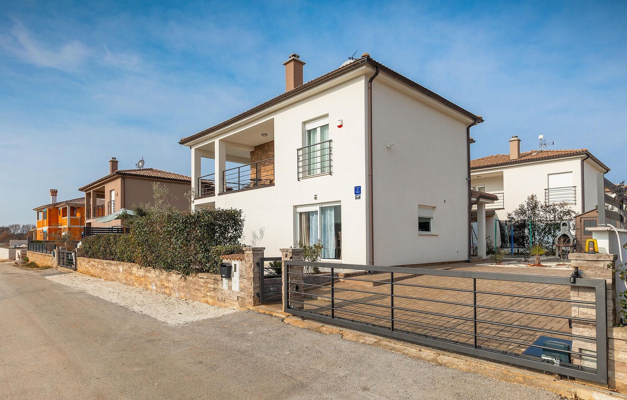 A two-story house with a balcony, a gated driveway, and a clear sky.