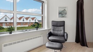 Une chambre moderne avec une grande fenêtre, une chaise noire, un radiateur et une affiche accrochée au mur.