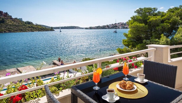 A balcony with a table set for breakfast, overlooking a lake with boats and a distant shoreline. - Lovely home in Rogoznica (Rogoznica)