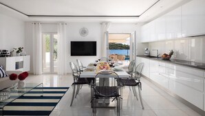 A modern, well-lit dining area with a large table set for a meal, surrounded by white cabinets and a kitchen area. - Lovely home in Rogoznica (Rogoznica)