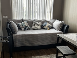 Un salon moderne avec un canapé gris, des coussins à motifs, une table basse en bois et une fenêtre avec des stores.