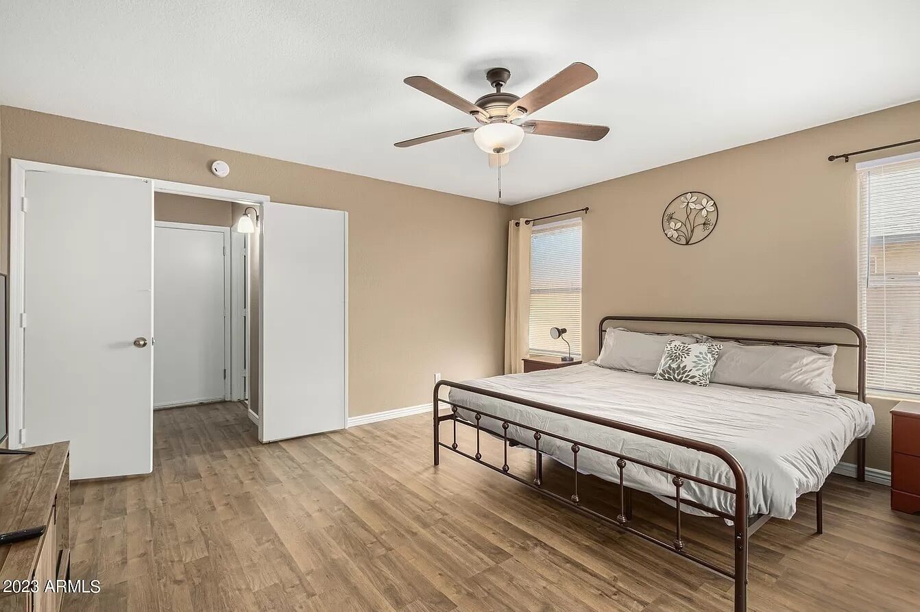 A bedroom with a bed, a ceiling fan, a nightstand, a window with blinds, and a door.