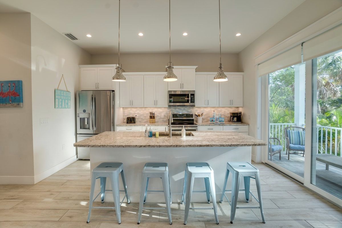 Una cocina moderna con una isla grande, taburetes de bar, luces colgantes y vistas a un balcón.