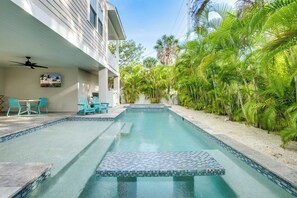 A swimming pool with a tiled deck, surrounded by palm trees and a building with a balcony.
