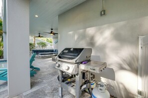 An outdoor patio area with a grill, seating, and a pool in the background.
