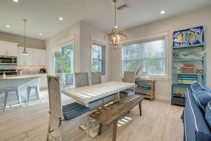 A modern kitchen with white cabinetry, a dining area with a wooden bench, and a view of the outdoors through large windows.