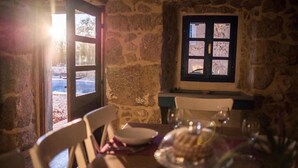Ein Zimmer mit Steinwänden, ein gedeckter Tisch, ein Fenster mit Blick und eine Tür, die nach draußen führt.
