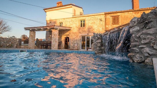 Ein Gebäude aus Stein mit Swimmingpool und Wasserfall.
