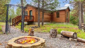A log cabin with a fire pit, wooden deck, and a metal gate.